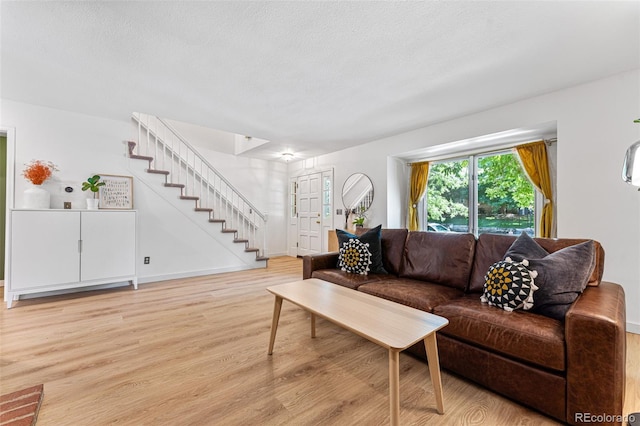 living room featuring light wood-style floors, stairs, baseboards, and a textured ceiling