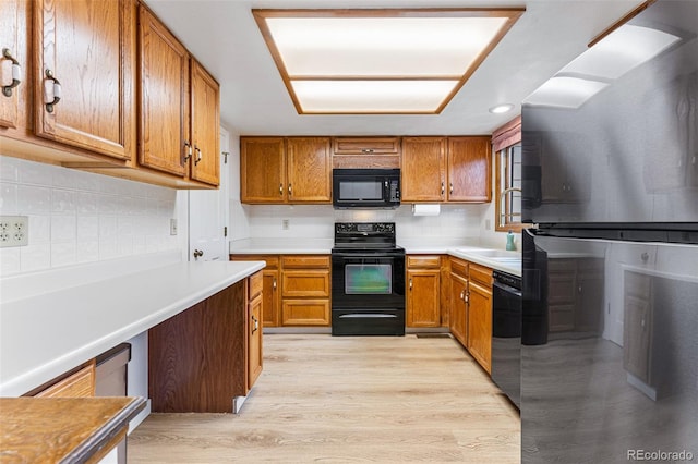 kitchen featuring black appliances, brown cabinetry, a sink, and light wood-style floors