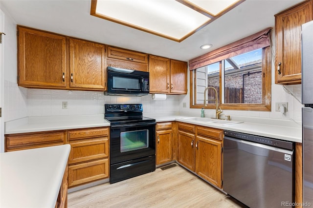 kitchen featuring a sink, light wood-style floors, backsplash, brown cabinets, and black appliances