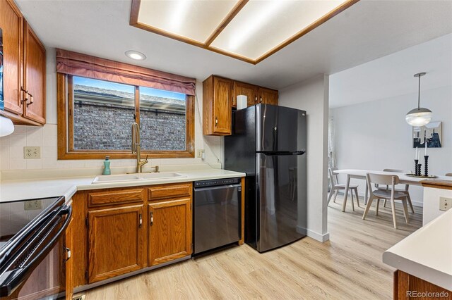 kitchen featuring light wood-style flooring, a sink, backsplash, black appliances, and brown cabinetry