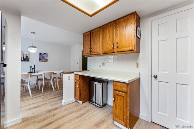 kitchen featuring light countertops, light wood finished floors, brown cabinetry, and tasteful backsplash