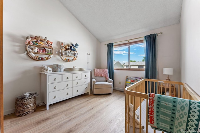 bedroom with baseboards, light wood-style floors, vaulted ceiling, a textured ceiling, and a nursery area