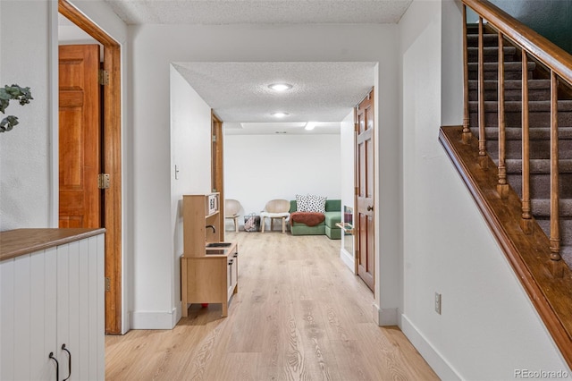 hallway with a textured ceiling, baseboards, stairs, and light wood-style floors