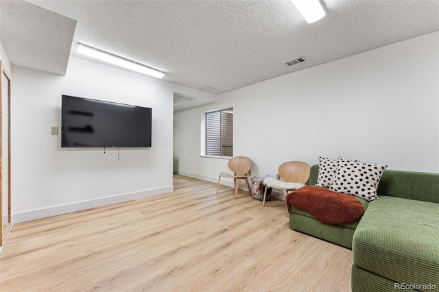 living room featuring visible vents, a textured ceiling, baseboards, and wood finished floors