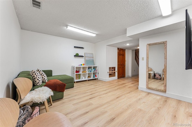 living area with visible vents, a textured ceiling, baseboards, and wood finished floors