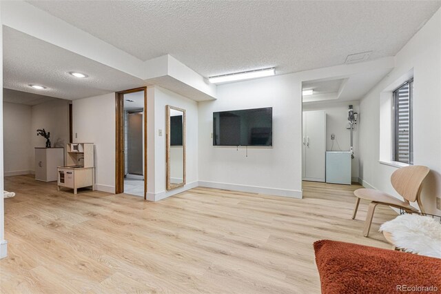 living room featuring baseboards, light wood-style flooring, and a textured ceiling