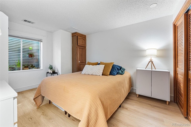 bedroom with a textured ceiling, light wood-style flooring, visible vents, and baseboards