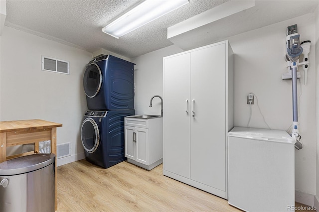 washroom featuring stacked washer / dryer, a sink, visible vents, light wood-type flooring, and cabinet space