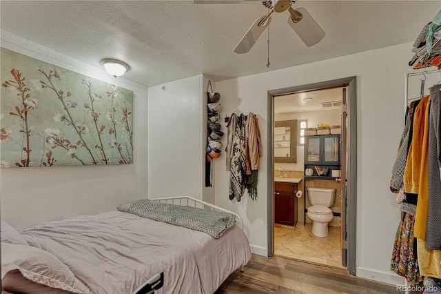 bedroom featuring ensuite bathroom, a ceiling fan, a textured ceiling, wood finished floors, and baseboards