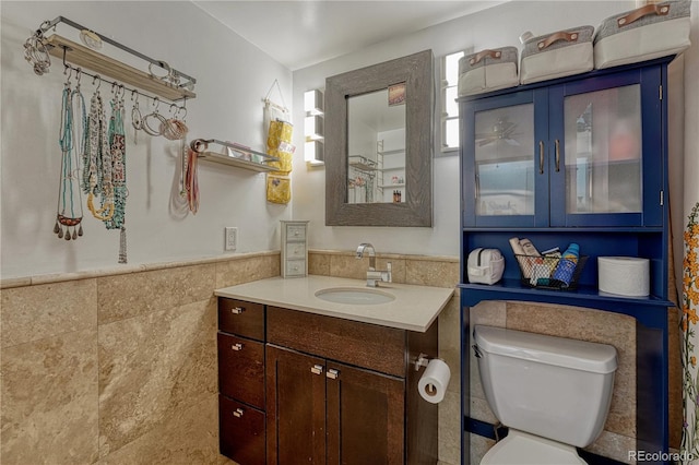 bathroom with toilet, vanity, tile walls, and wainscoting