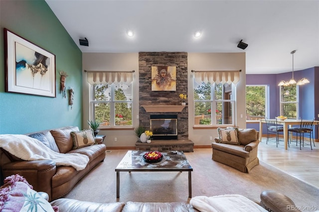 carpeted living room featuring a chandelier and a stone fireplace