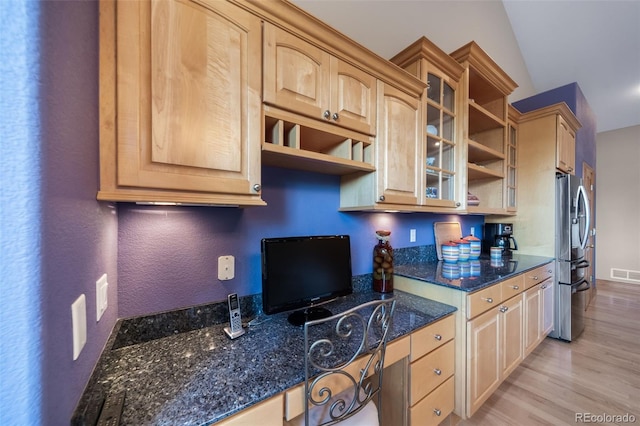 kitchen with light brown cabinets, vaulted ceiling, and dark stone countertops