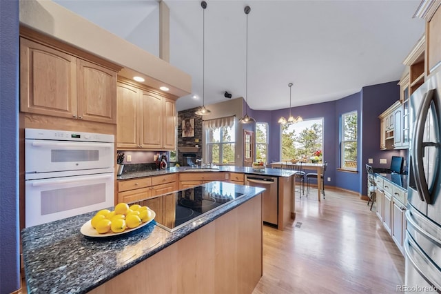 kitchen with appliances with stainless steel finishes, decorative light fixtures, dark stone countertops, kitchen peninsula, and light hardwood / wood-style flooring