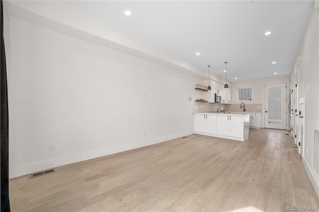 kitchen featuring light wood-type flooring, open shelves, white cabinets, light countertops, and decorative backsplash