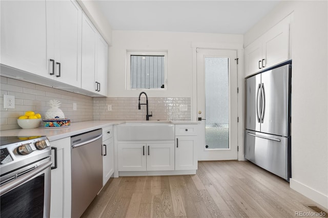 kitchen with light wood-style flooring, backsplash, white cabinets, and appliances with stainless steel finishes