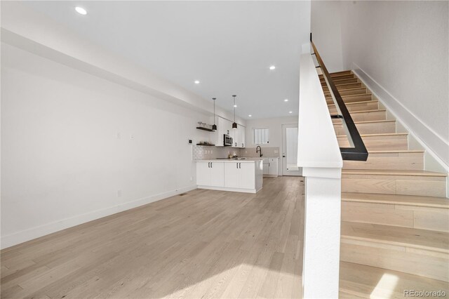 unfurnished living room with stairway, recessed lighting, light wood-style flooring, and baseboards