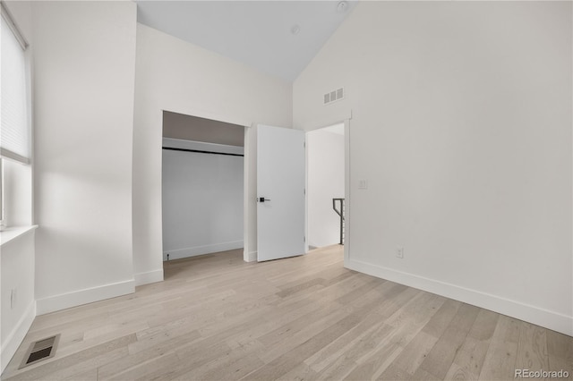 unfurnished bedroom featuring light wood-type flooring, visible vents, baseboards, and high vaulted ceiling