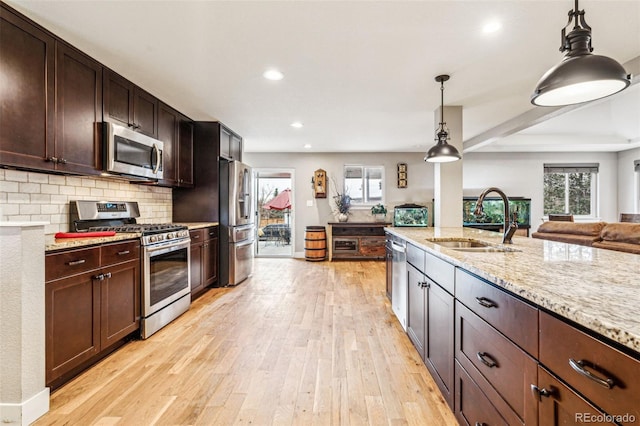 kitchen featuring light wood finished floors, appliances with stainless steel finishes, open floor plan, and a sink