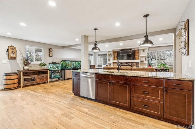 kitchen with a sink, light wood finished floors, open floor plan, stainless steel dishwasher, and light stone countertops