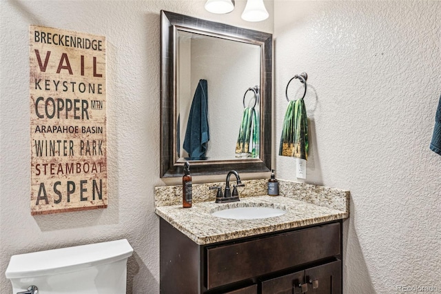 bathroom with vanity, toilet, and a textured wall