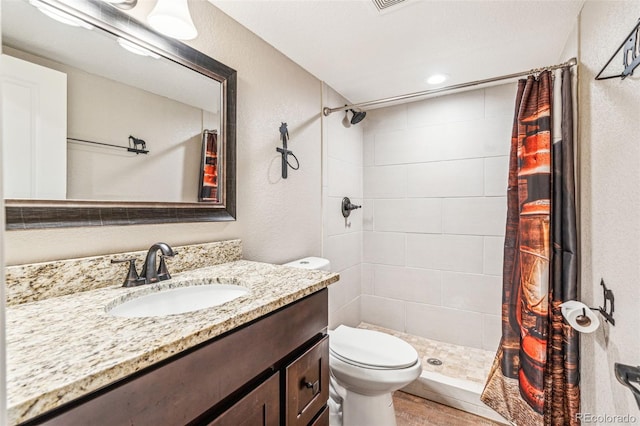 bathroom featuring vanity, toilet, a textured wall, and a shower stall