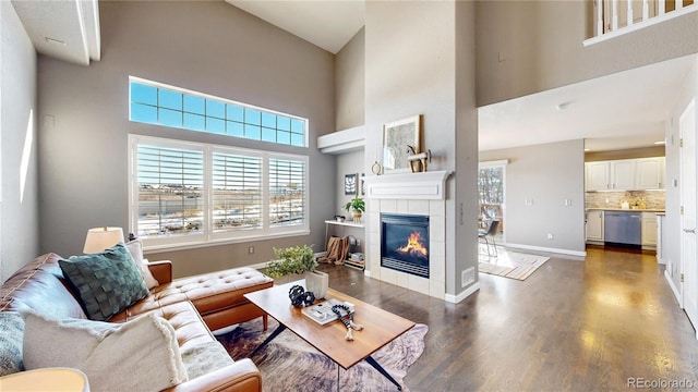 living room with a tile fireplace, a towering ceiling, and dark wood-type flooring