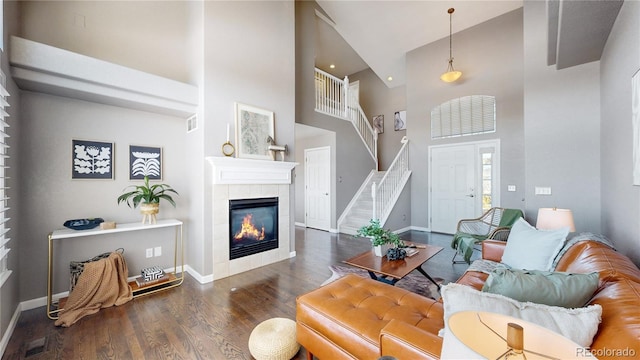 living room featuring a tiled fireplace, dark hardwood / wood-style flooring, and a towering ceiling