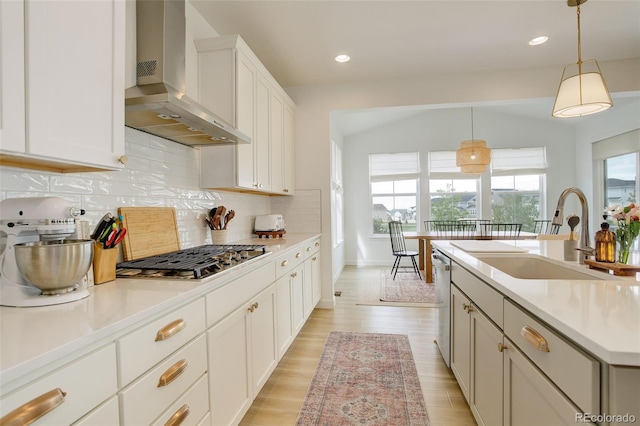 kitchen featuring wall chimney range hood, appliances with stainless steel finishes, a sink, tasteful backsplash, and light countertops