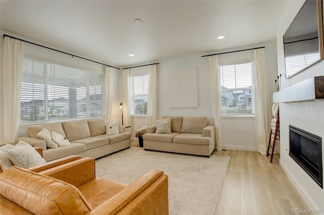 living room with light wood finished floors, a glass covered fireplace, baseboards, and recessed lighting