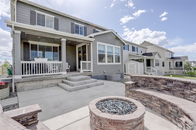 back of house with an outdoor fire pit, covered porch, a storage unit, an outbuilding, and a patio