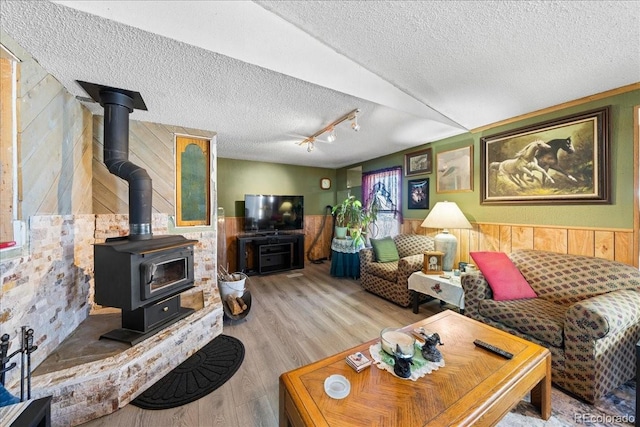 living area with a wood stove, a wainscoted wall, a textured ceiling, and wood finished floors