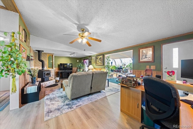 living area featuring a textured ceiling, ceiling fan, light wood finished floors, and a wood stove