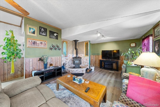 living area with a wood stove, a wainscoted wall, a textured ceiling, and wood finished floors