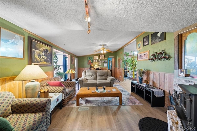 living area with a textured ceiling, vaulted ceiling, wood finished floors, and wainscoting