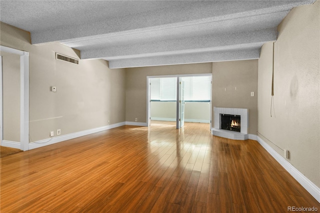 unfurnished living room with baseboards, visible vents, a fireplace, and hardwood / wood-style floors