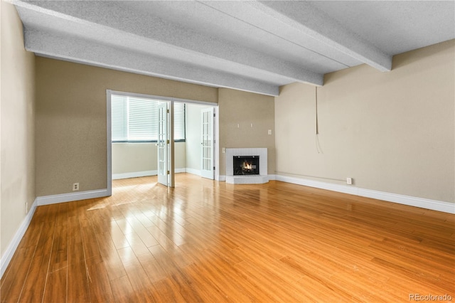 unfurnished living room with light wood finished floors, baseboards, a textured ceiling, a fireplace, and beam ceiling