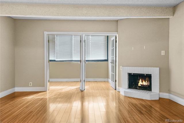 unfurnished living room with a brick fireplace, baseboards, and light wood-style floors