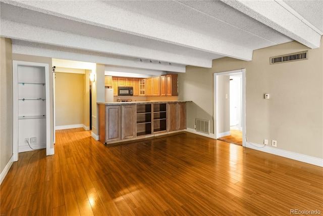 unfurnished living room with baseboards, visible vents, dark wood-type flooring, and beamed ceiling