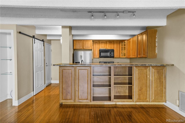 kitchen with a barn door, brown cabinetry, glass insert cabinets, freestanding refrigerator, and black microwave