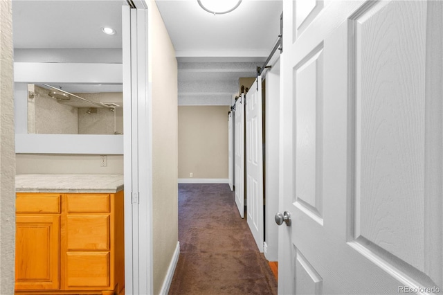 corridor featuring a barn door, baseboards, and dark colored carpet