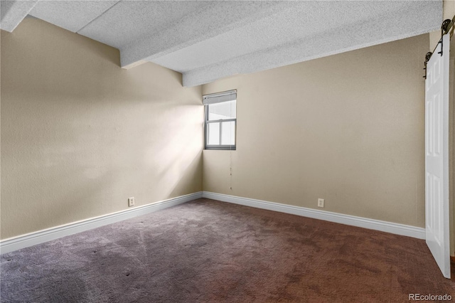 carpeted spare room featuring a textured ceiling, a barn door, and baseboards