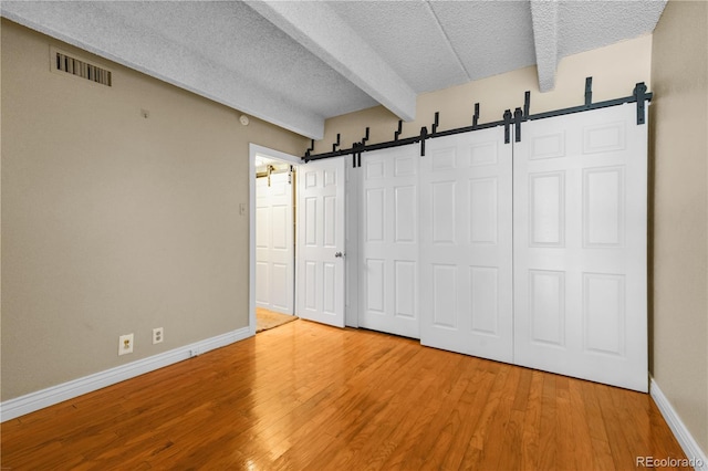 unfurnished bedroom featuring a barn door, a textured ceiling, visible vents, and beam ceiling