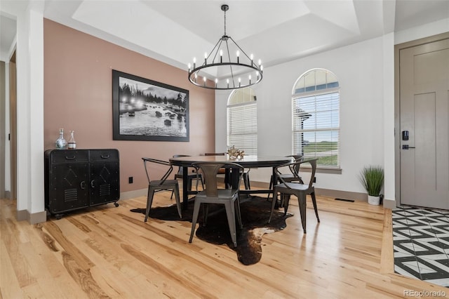 dining area featuring light wood finished floors, a chandelier, a raised ceiling, and baseboards