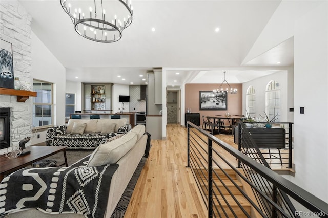 living room with a chandelier, light wood finished floors, a fireplace, and high vaulted ceiling