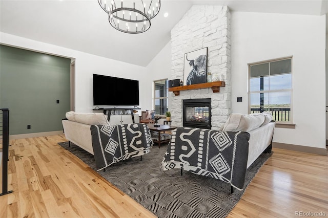 living area with a chandelier, high vaulted ceiling, a stone fireplace, wood finished floors, and baseboards