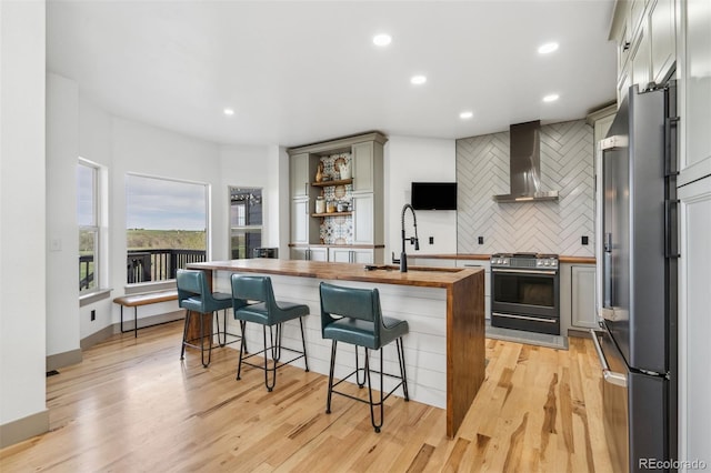 kitchen featuring range with gas cooktop, butcher block countertops, freestanding refrigerator, wall chimney exhaust hood, and tasteful backsplash