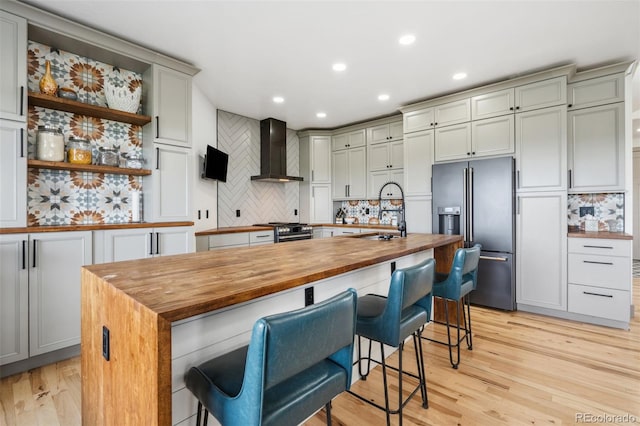 kitchen featuring butcher block counters, wall chimney exhaust hood, high end appliances, a sink, and tasteful backsplash