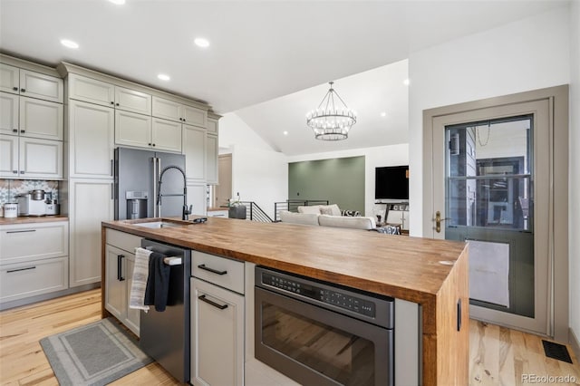kitchen with butcher block counters, a sink, appliances with stainless steel finishes, light wood-style flooring, and vaulted ceiling
