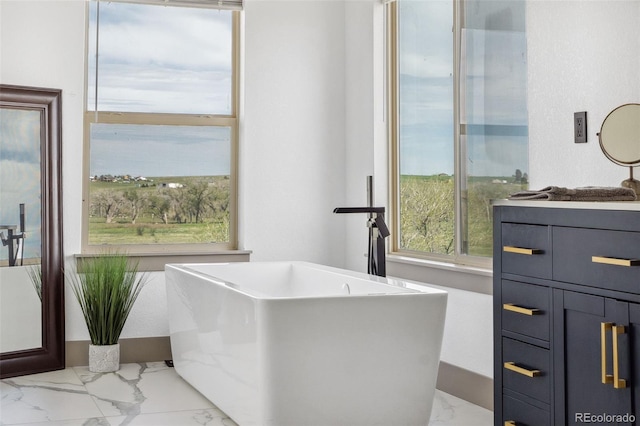 bathroom with marble finish flooring, vanity, and a freestanding tub