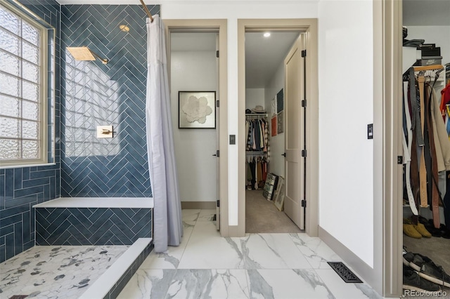 full bathroom featuring a tile shower, marble look tiles, baseboards, and a walk in closet